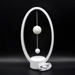 Candeeiro de mesa com estrutura oval branca, duas esferas suspensas e base circular, com cabo de alimentação junto.