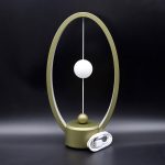 Candeeiro de mesa com estrutura oval dourada, esfera branca suspensa no centro e base redonda dourada, com cabo de alimentação junto.