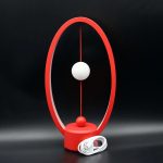 Lâmpada de mesa com estrutura circular vermelha, esfera branca suspensa e base circular vermelha, com cabo de energia branco.