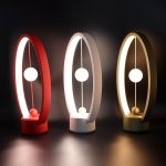 Três candeeiros de mesa Heng Balance em cores diferentes: vermelho, branco e dourado, com design moderno e iluminação suave, colocados sobre uma superfície escura.