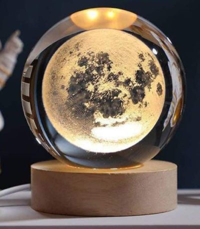 Lâmpada de mesa em forma de lua com iluminação suave, apoiada numa base de madeira, ideal para decoração de quarto ou escritório.