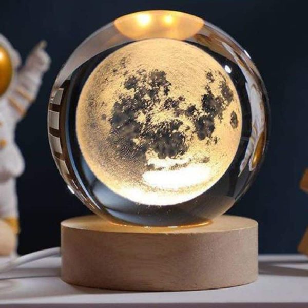Lâmpada de mesa em forma de lua com iluminação suave, apoiada numa base de madeira, ideal para decoração de quarto ou escritório.