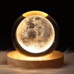 Candeeiro de mesa em forma de lua com iluminação suave, apoiado numa base de madeira circular, ideal para decoração de ciência e ambiente relaxante.