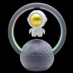 Candeeiro de mesa com figura de astronauta branco, cabeça dourada e luz LED colorida ao redor, apoiado numa réplica da Lua, ideal para decoração científica.