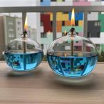Duas lâmpadas de plasma redondas com filamentos acesos, colocadas numa superfície de madeira, com edifícios coloridos ao fundo.