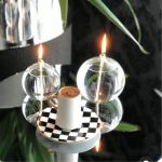 Candeeiro de mesa com base de vidro transparente, lâmpadas acesas, e uma chávena de café em cima de um prato de padrão xadrez.