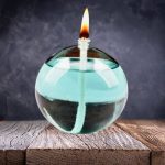 Velas de óleo em recipiente de vidro redondo, com chama acesa, sobre uma superfície de madeira, fundo escuro.