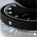 Relógio de luz com mostrador digital, destaque para o botão de power na lateral, com iluminação branca e detalhes em preto.