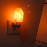 Lâmpada de sal emite luz quente, com cristais visíveis e efeito de brilho na parede ao lado.