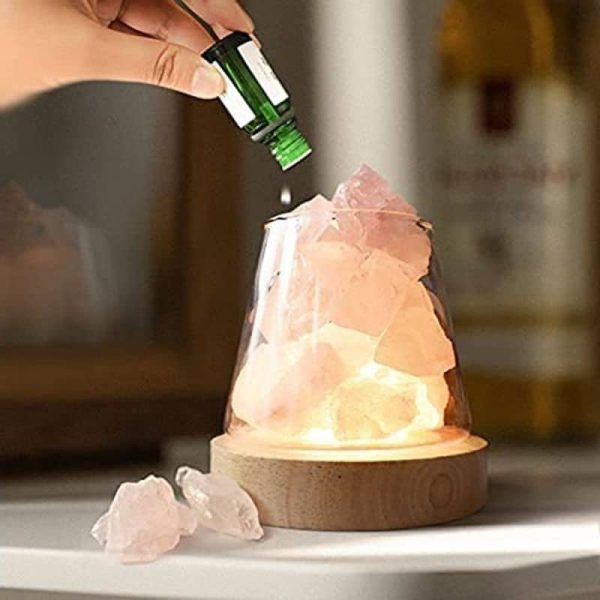 Pessoa a colocar óleo essencial numa lâmpada de sal rosa dos Himalaias, com pedaços de sal ao lado.