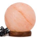 Candeeiro de sal em forma de esfera, com iluminação suave, apoiado numa base de madeira escura, com cabo elétrico visível ao lado.