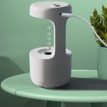 Lâmpada de plasma com design moderno, exibindo filamentos de plasma visíveis e uma base branca, conectada por um cabo elétrico, colocada numa mesa verde.