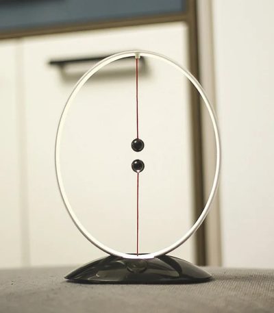 Pendulo de Newton com duas bolas pretas suspensas por fios finos dentro de um aro metálico, sobre uma superfície plana.