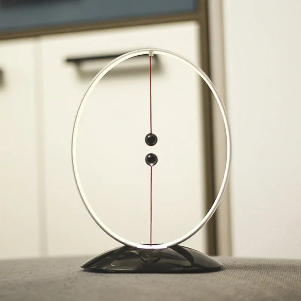 Pendulo de Newton com duas bolas pretas suspensas por fios finos dentro de um aro metálico, sobre uma superfície plana.