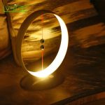 Candeeiro de mesa com design circular, iluminação suave e base de apoio, em ambiente escuro, destacando-se pelo seu estilo moderno e funcionalidade.