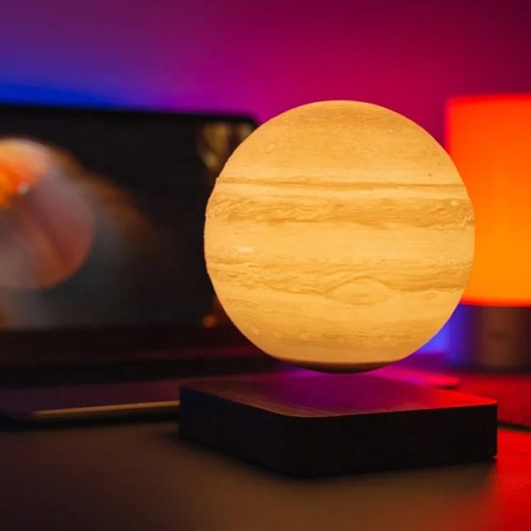Lâmpada de planeta Júpiter com detalhes de texturas e cores, iluminada com luz quente, colocada sobre uma base preta, com fundo colorido difuso.