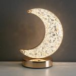 Luminária de lua em acrílico com detalhes brilhantes, base metálica dourada, iluminação suave, ideal para decoração de quarto ou sala.