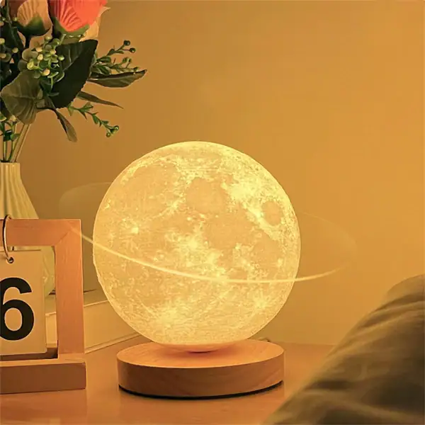 Candeeiro em forma de lua com iluminação amarelada, colocado numa base de madeira, decorando uma sala com plantas e objetos de decoração.