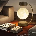 Candeeiro lunar em forma de esfera iluminada, com base e braço curvo, colocado ao lado de livros e objetos decorativos numa sala moderna.