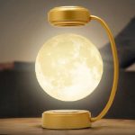 Candeeiro lunar em miniatura com base e braço dourados, luz LED que simula a superfície lunar, ideal para decoração de ciência e iluminação ambiente.