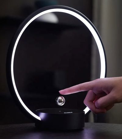 Lâmpada de plasma circular com anel de luz LED e esfera suspensa, manipulada por uma mão, em ambiente escuro.