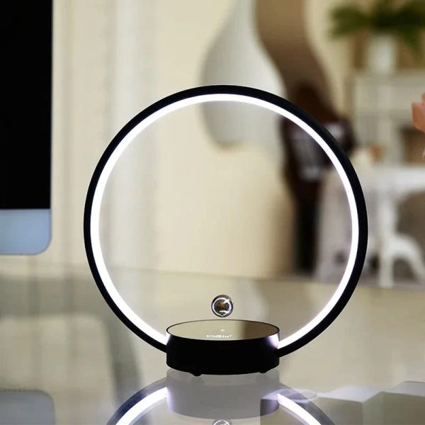 Candeeiro circular com luz LED branca, base preta e esfera metálica suspensa no centro, em ambiente de sala moderna.
