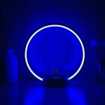 Candeeiro circular com luz LED azul, base preta, em ambiente escuro, com efeito de iluminação circular.