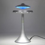 Candeeiro com design futurista em forma de disco voador, com luz azul e base metálica, em funcionamento numa superfície plana.