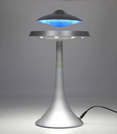 Candeeiro com design futurista em forma de disco voador, com luz azul e base metálica, em funcionamento numa superfície plana.