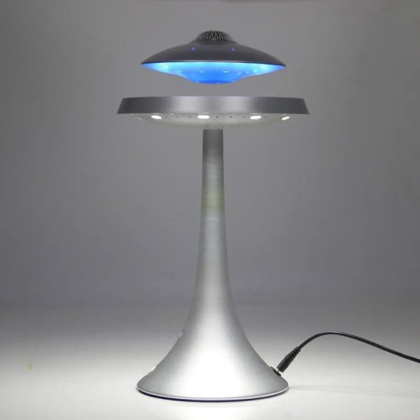 Candeeiro com design futurista em forma de disco voador, com luz azul e base metálica, em funcionamento numa superfície plana.