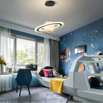 Quarto infantil decorado com tema espacial, parede pintada com planetas e estrelas, cama com design de nave espacial, iluminação moderna com lâmpada de anel e planeta.