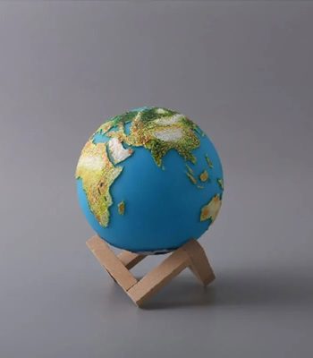 Mini globo terrestre com relevo detalhado, apoiado num suporte de madeira simples, sobre fundo cinzento.