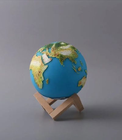 Mini globo terrestre com relevo detalhado, apoiado num suporte de madeira simples, sobre fundo cinzento.