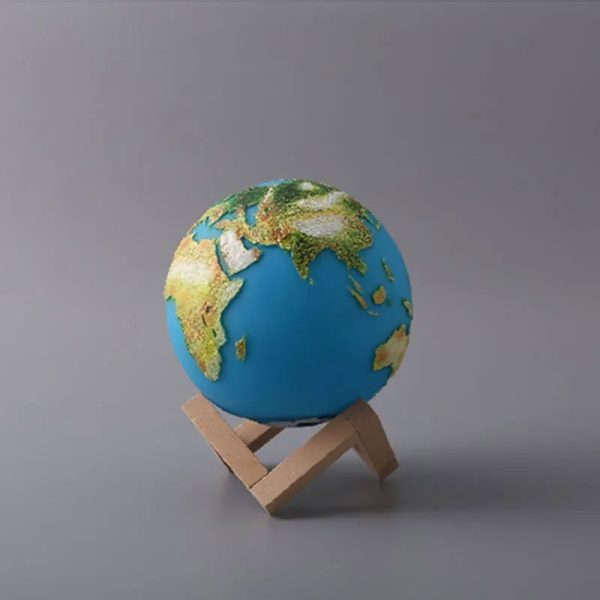 Mini globo terrestre com relevo detalhado, apoiado num suporte de madeira simples, sobre fundo cinzento.