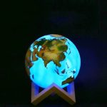 Lâmpada decorativa em forma de planeta Terra com continentes visíveis, iluminada com luz azul, colocada numa base de suporte.