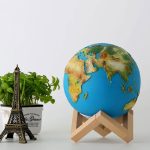 Globo terrestre decorativo com cores vibrantes, apoiado num suporte de madeira, ao lado de uma planta em vaso e uma miniatura da Torre Eiffel.