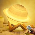 Luminária em forma de Saturno com anel iluminado, apoiada numa base de madeira, com controlo remoto na mão ao lado.