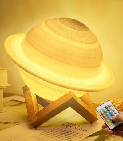 Luminária em forma de Saturno com anel iluminado, apoiada numa base de madeira, com controlo remoto na mão ao lado.