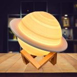 Lâmpada de Saturno com anéis, iluminada, sobre suporte de madeira, ambiente de loja de gadgets científicos.