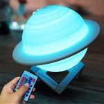Lâmpada em forma de Saturno iluminada com luz azul, apoiada numa base de madeira, controlada por um comando remoto com botões coloridos.