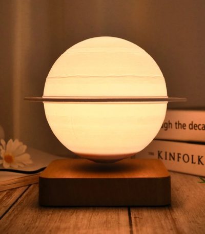 Candeeiro com forma de Saturno, com anel metálico ao redor, iluminado, sobre base de madeira, ambiente acolhedor.
