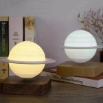 Candeeiro de mesa com design de planeta Saturno, luz amarela e branca, base de madeira, decorativo para ambientes científicos ou educativos.