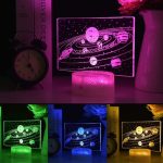 Lâmpada 3D com ilustração do sistema solar, iluminada em cor rosa, com base de LED. Mostra planetas e órbitas em detalhes.