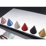 Cones giroscópicos metálicos de cores diferentes, dispostos numa linha sobre uma superfície branca, com destaque para o acabamento brilhante e cores vibrantes.