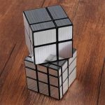 Duas peças de Cubo de Rubik Espelho empilhadas, uma com faces refletoras e outra com acabamento escuro, sobre uma superfície de madeira.