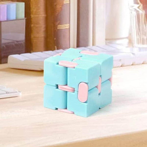 Cubo fidget infinito com blocos azuis e detalhes rosa, mostrado numa mesa de madeira clara, com fundo de estantes e objetos de escritório.