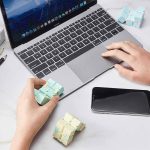 Pessoa a manipular um cubo fidget infinito com várias cores, junto de um portátil e smartphone numa mesa de trabalho.