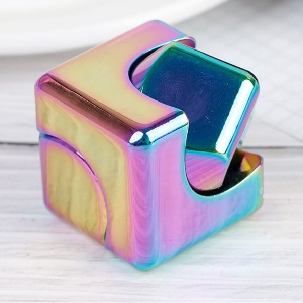 Cubo fidget com acabamento holográfico, superfície lisa e cores iridescentes, mostrado numa mesa de madeira clara, com detalhes de reflexão e brilho.