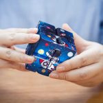 Pessoa a segurar um cubo infinito com tema espacial, ilustrado com astronauta, planetas e estrelas, em cores vibrantes e detalhes detalhados.