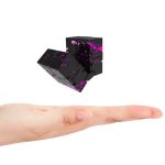 Cubo de aço preto com pintura rosa e roxa, flutuando acima de uma mão aberta, mostrando detalhes da pintura e do design do cubo.